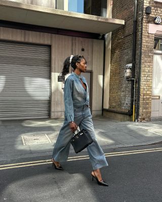 A woman wears a a denim top, jeans, black slingbacks, and a black hermes bag.