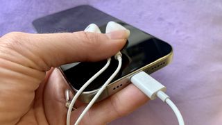 Écouteurs USB-C connectés à un iPhone 15, tenu dans une main, sur fond violet