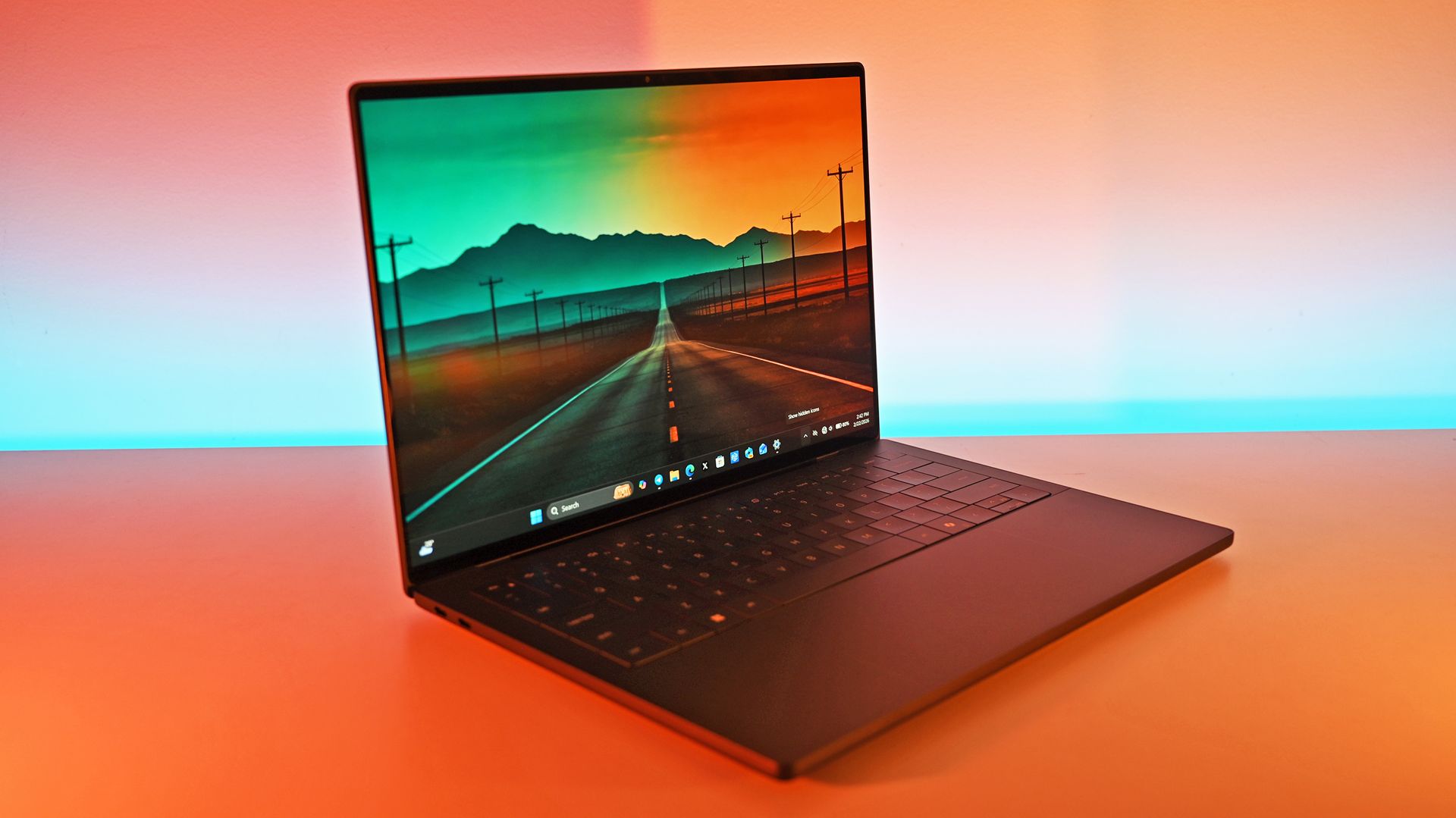 A dark gray Dell XPS 14 laptop open on a table showing a wallpaper of an open road stretching toward mountains, illuminated by ambient warm light.