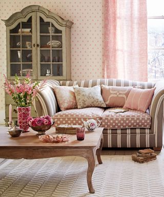 Pink living room with taupe and beige stripe sofa and French armour display cabinet