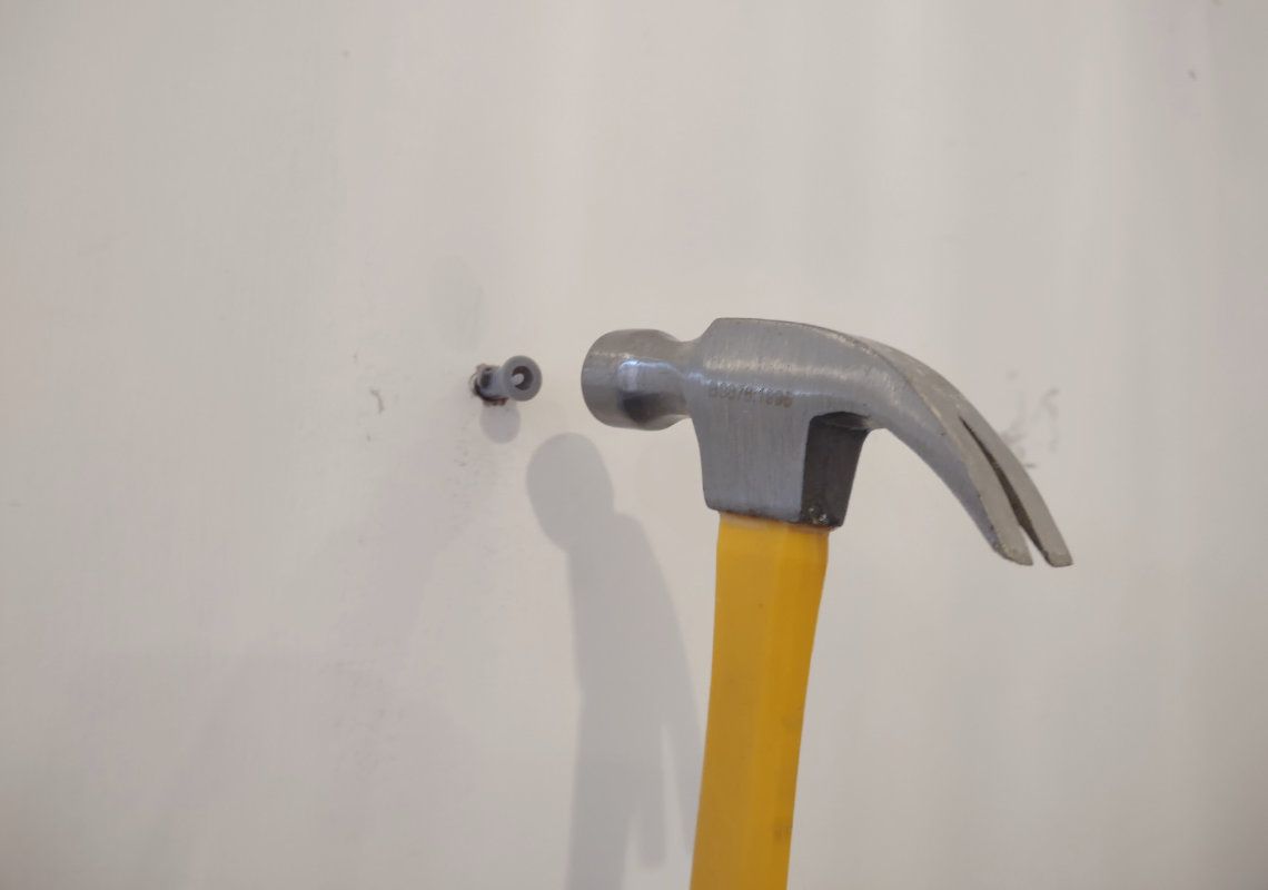 A hammer being used on a screw plug in a white wall