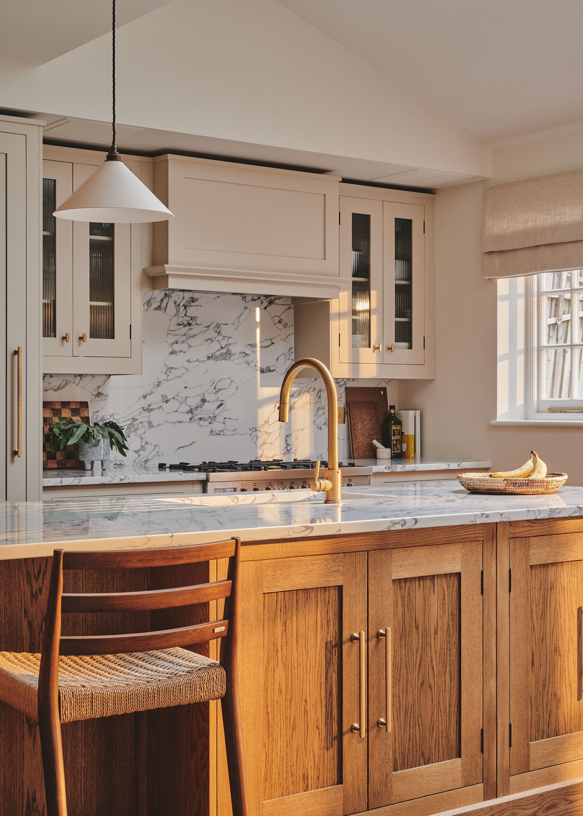 A kitchen with townhouse features, a stone island, wooden cabinets, a woven stool, and a single pendant