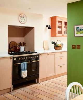 A kitchen with light pink frameless kitchen cabinets, wooden flooring, and a bright green feature wall