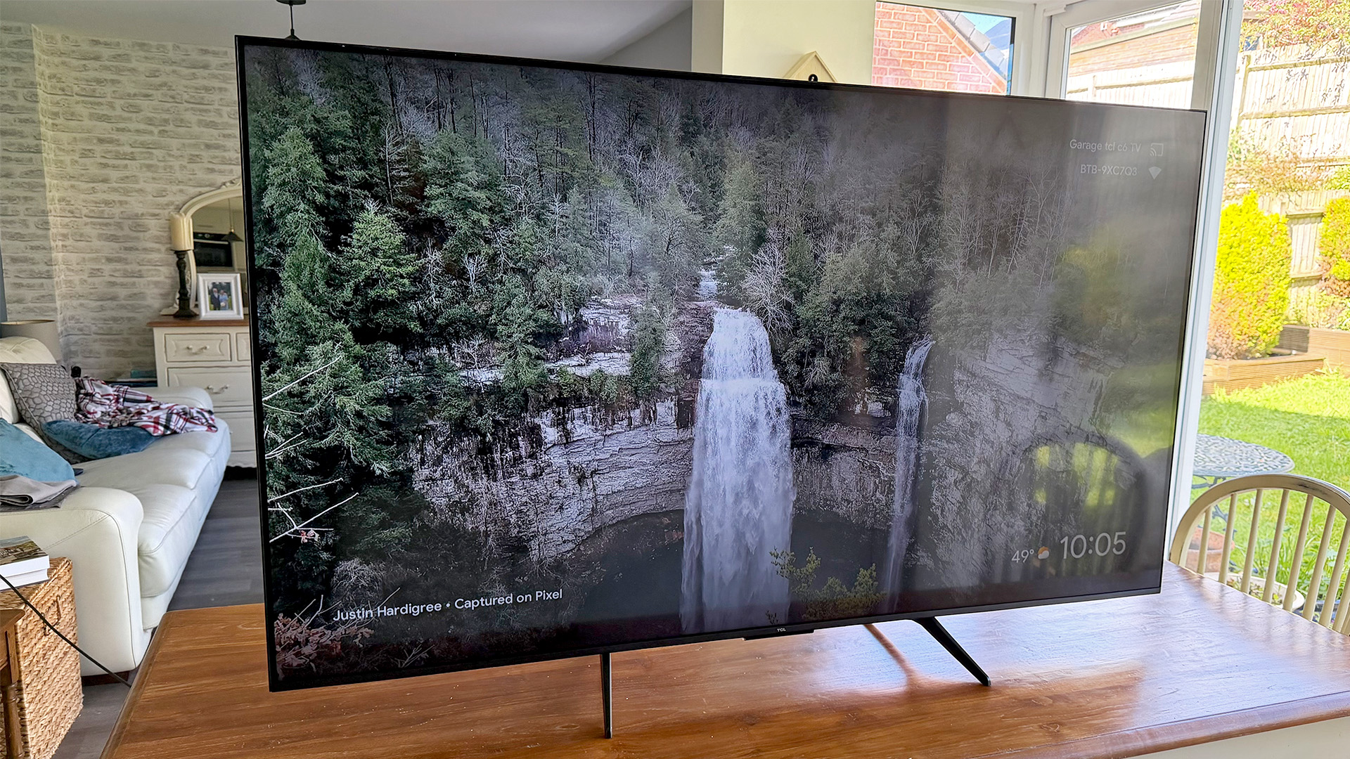 TCL Q6C 65-inch LCD TV on wooden dining table, on screen is waterfall
