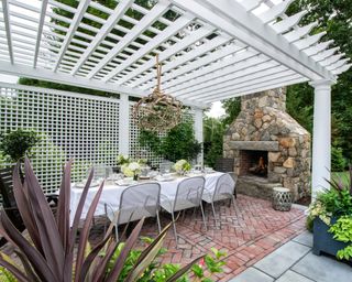 An outdoor dining area with white pergola, trellis, and outdoor fireplace