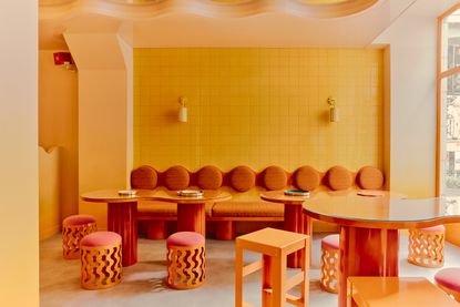 banquette seating with circular backrests in a row and circular tables with circular stools and curves and waves in the design in a bold and bright orange, yellow, and pink color palette