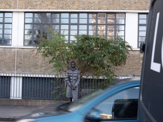 Man on road in puffer jacket with apartment block in background