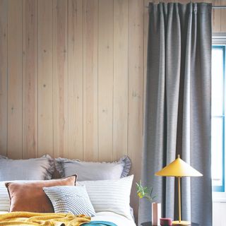 A bedroom with wood wall panelling and a window next to the bed with grey curtains