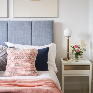 bed with blue headboard, cushions in front and a side table with gold lamp on