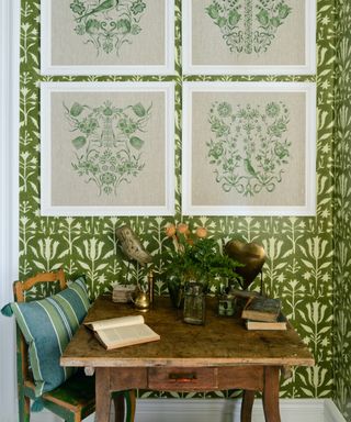 Small dining space alcove with green wallpaper, vintage table and chair, four embroidery style artworks, vintage pieces