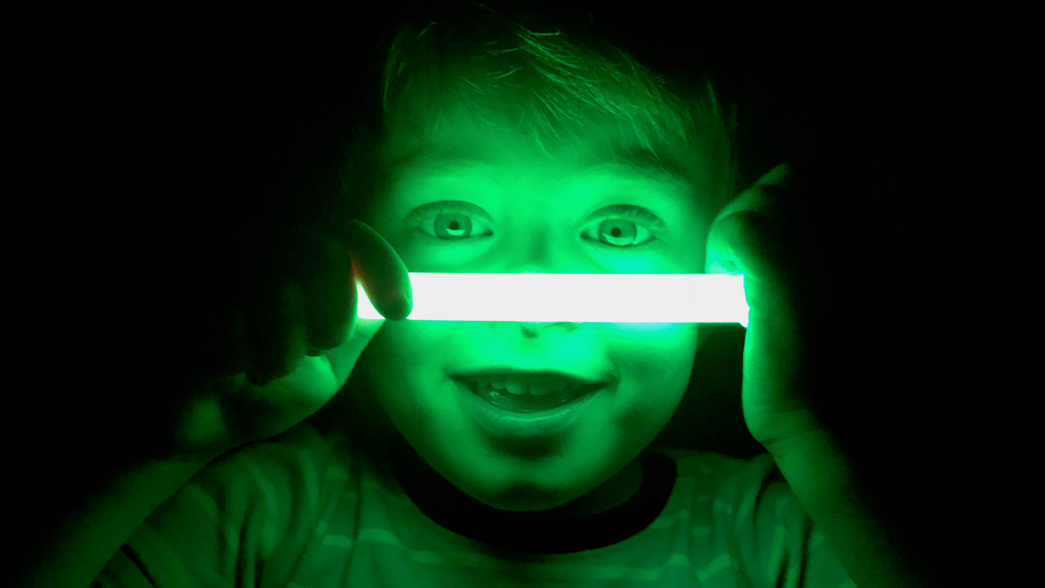 Young child holding a green glow stick up to their face