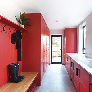 Red utility room with white ceramic sink, boot bench and grey floor tiles