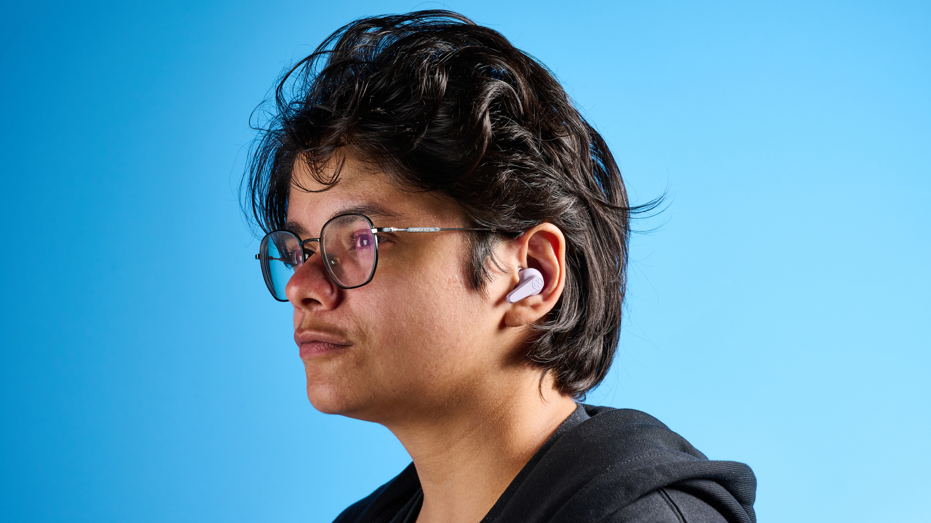 the jlab go pods anc earbuds in lilac with a lilac charging case and built in usb-c cable against a blue background on a marble stand