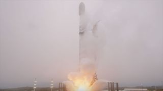 a black and white rocket lifts off into an overcast, foggy sky, its thrust lighting the landscape below