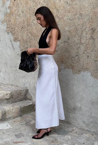 A woman wearing a black halter top with a white maxi skirt, black strappy sandals, and a snakeskin clutch bag.