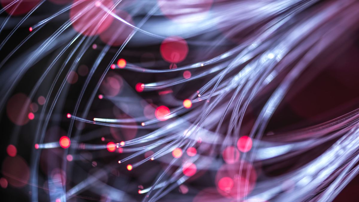 A close-up shot of a bundle of fibre optic cables, with red light shining through each cable