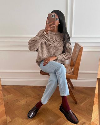 fashion influencer @symphonyofsilk wearing a brown sweater, blue jeans, red socks, and black loafers