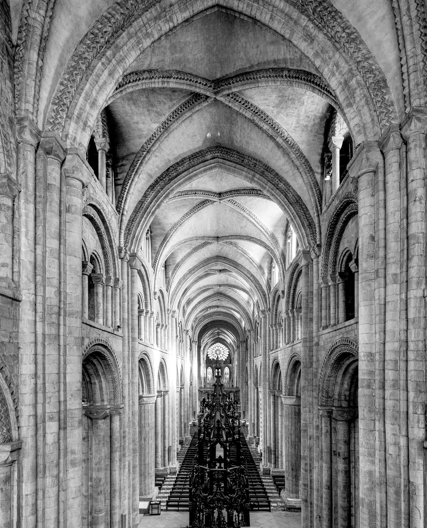 Gothic church interior featuring tall, intricately designed arches, stone walls, and ornate chandeliers in a dramatic black and white