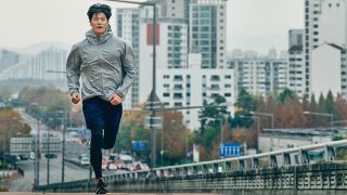 Man running in city wearing running tights and shorts, and running jacket