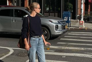 Clara wears a black sweater, blue jeans, a black belt, brown leather shoulder bag, and black ballet flats.