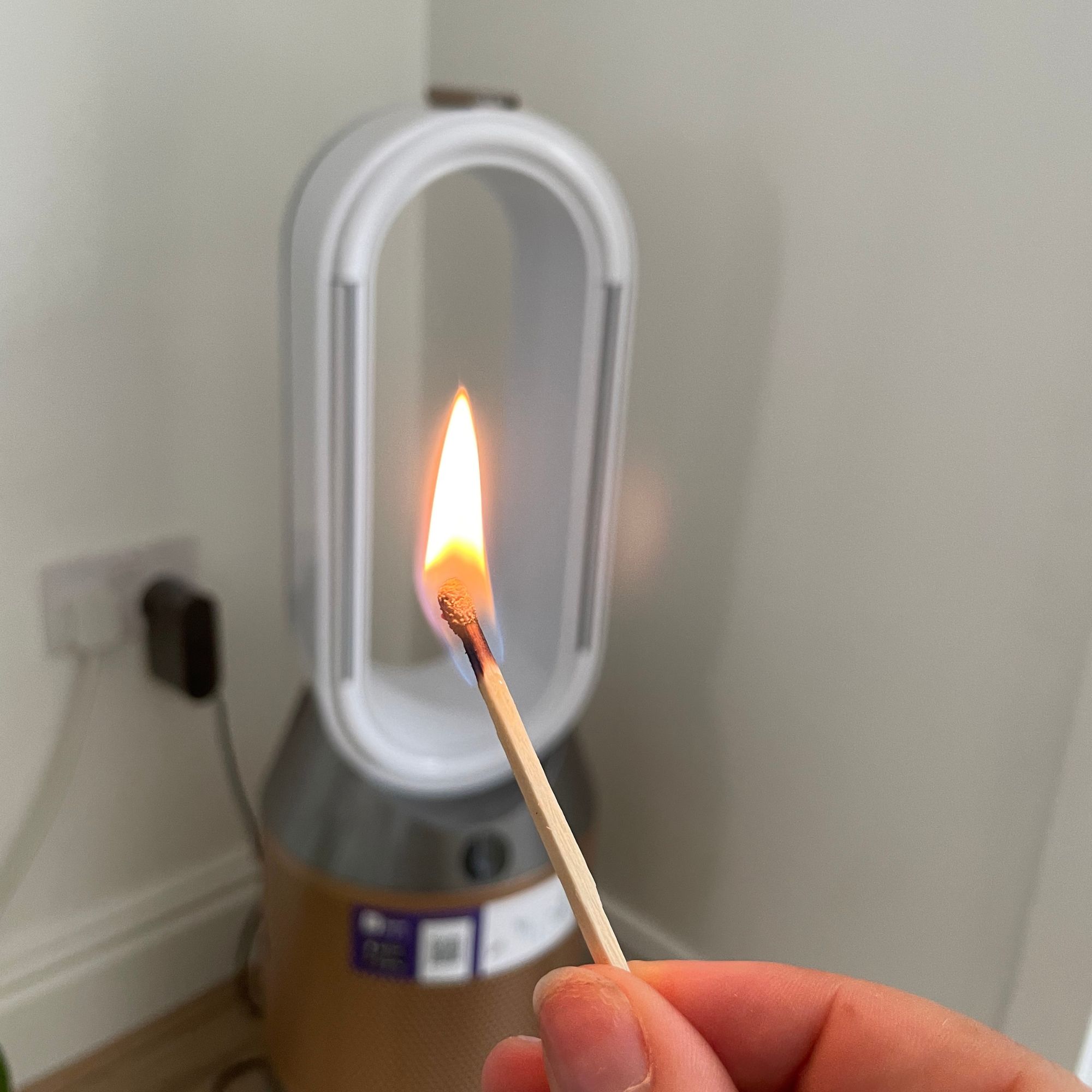 Hand holding a lit match in front of the Dyson Purifier Humidify+Cool PH2 De-Nox