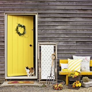 house having wooden walls yellow door and bench with cushions infront
