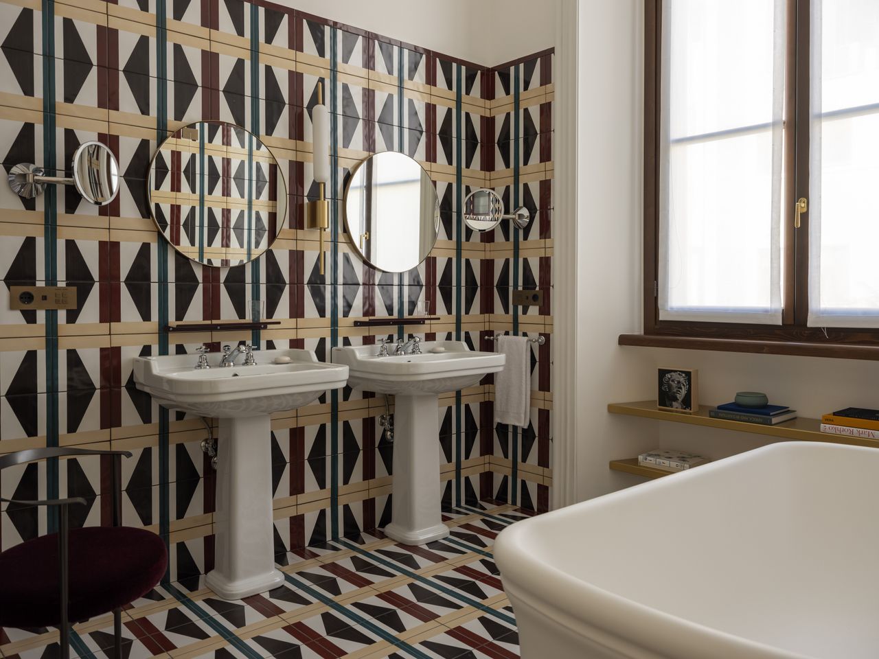 A 1980s-inspired bathroom features colorful tiled walls including geometric motifs in the tones of yellow, green, cream, and burgundy.