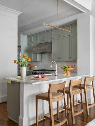 A muted green and white kitchen with small peninsula and wooden bar stools