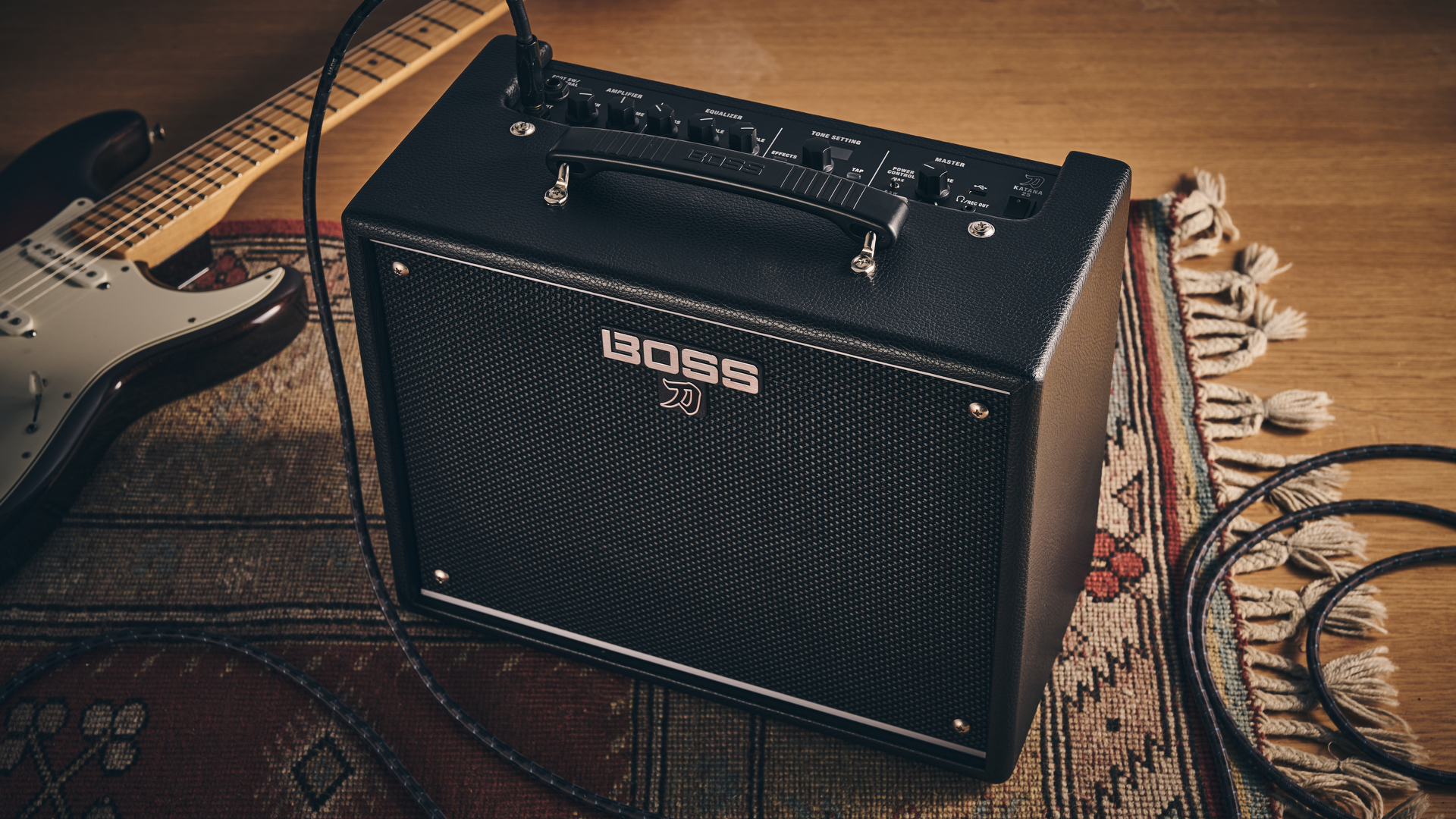 A Boss Katana-25 practice amp on a rug with an electric guitar in the background