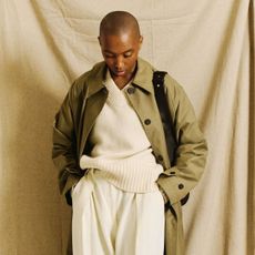 Marisa wears a green trench coat, cream jumper and cream trousers