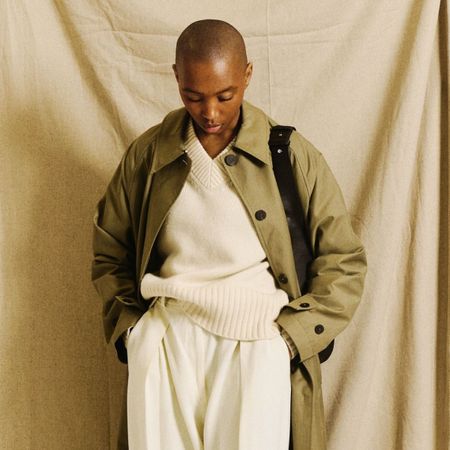 Marisa wears a green trench coat, cream jumper and cream trousers