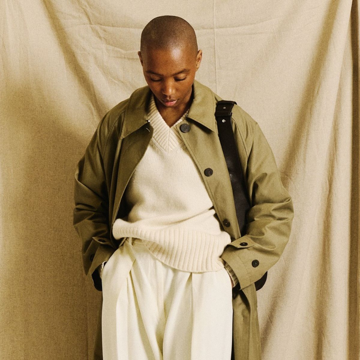 Marisa wears a green trench coat, cream jumper and cream trousers