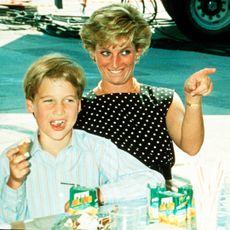 Princess Diana pointing and laughing at a table next to Prince William, who is eating
