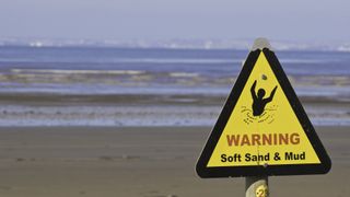 A yellow quicksand warning sign at the beach