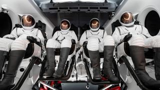 four people in white spacesuits with gold visors sit inside a white spacecraft cabin