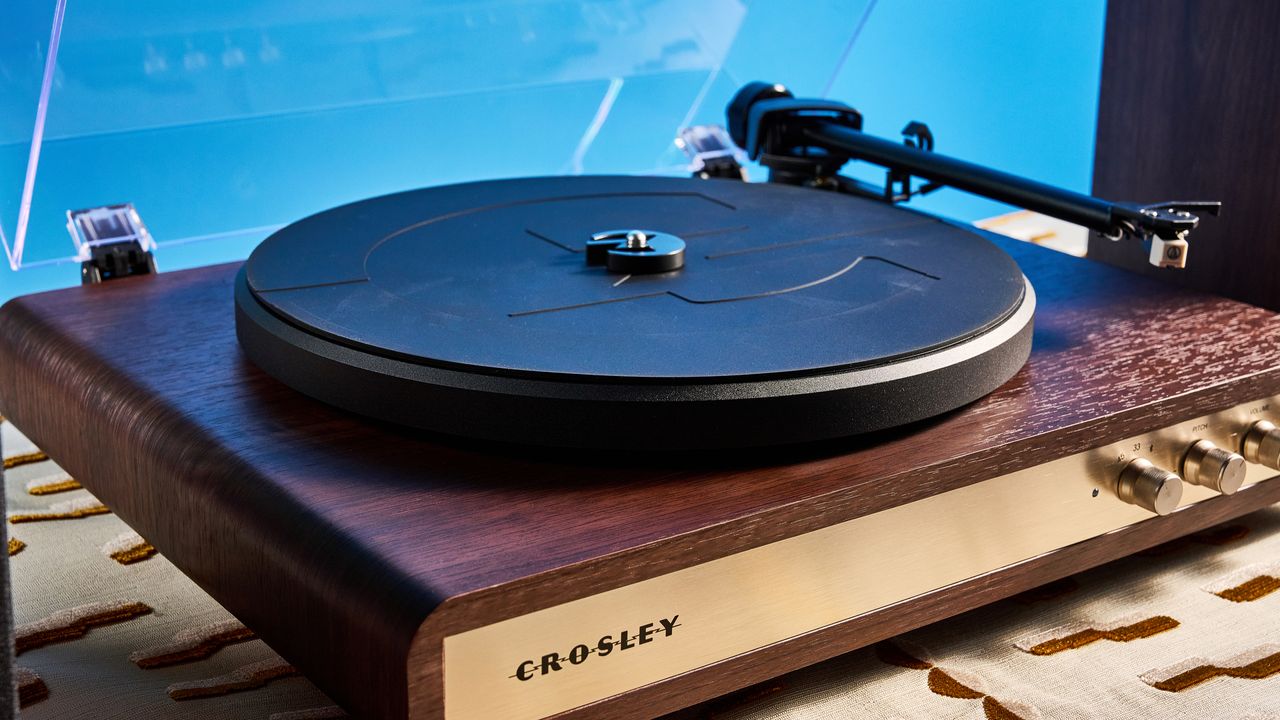 Crosley C65 turntable and bookshelf speakers photographed in front of a blue background on a brown table.