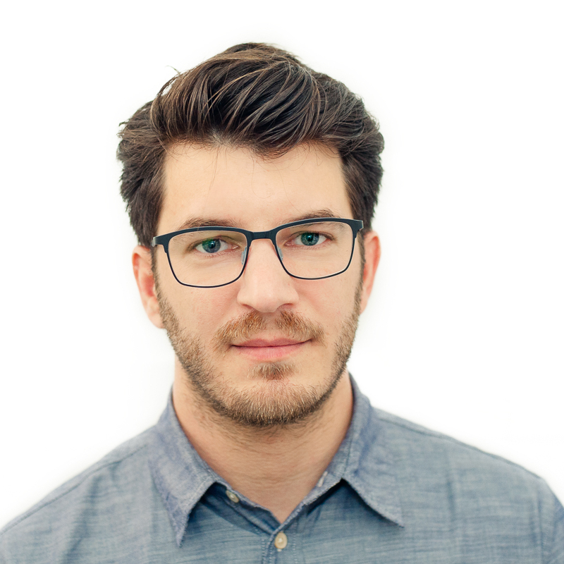 male with short wavy brown hair, wearing glasses and blue denim like shirt