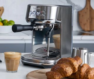 Breville Bambino Plus on a countertop with croissants and a coffee in front
