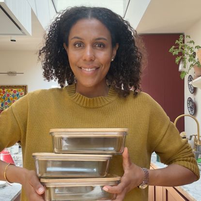 Woman standing in kitchen holding stack of three stainless steel food storage containers