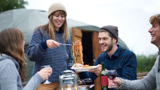 Woman handing out spaghetti with a ladle to friends on camping trip