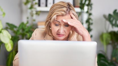 An older woman looks stressed as she looks at her laptop.