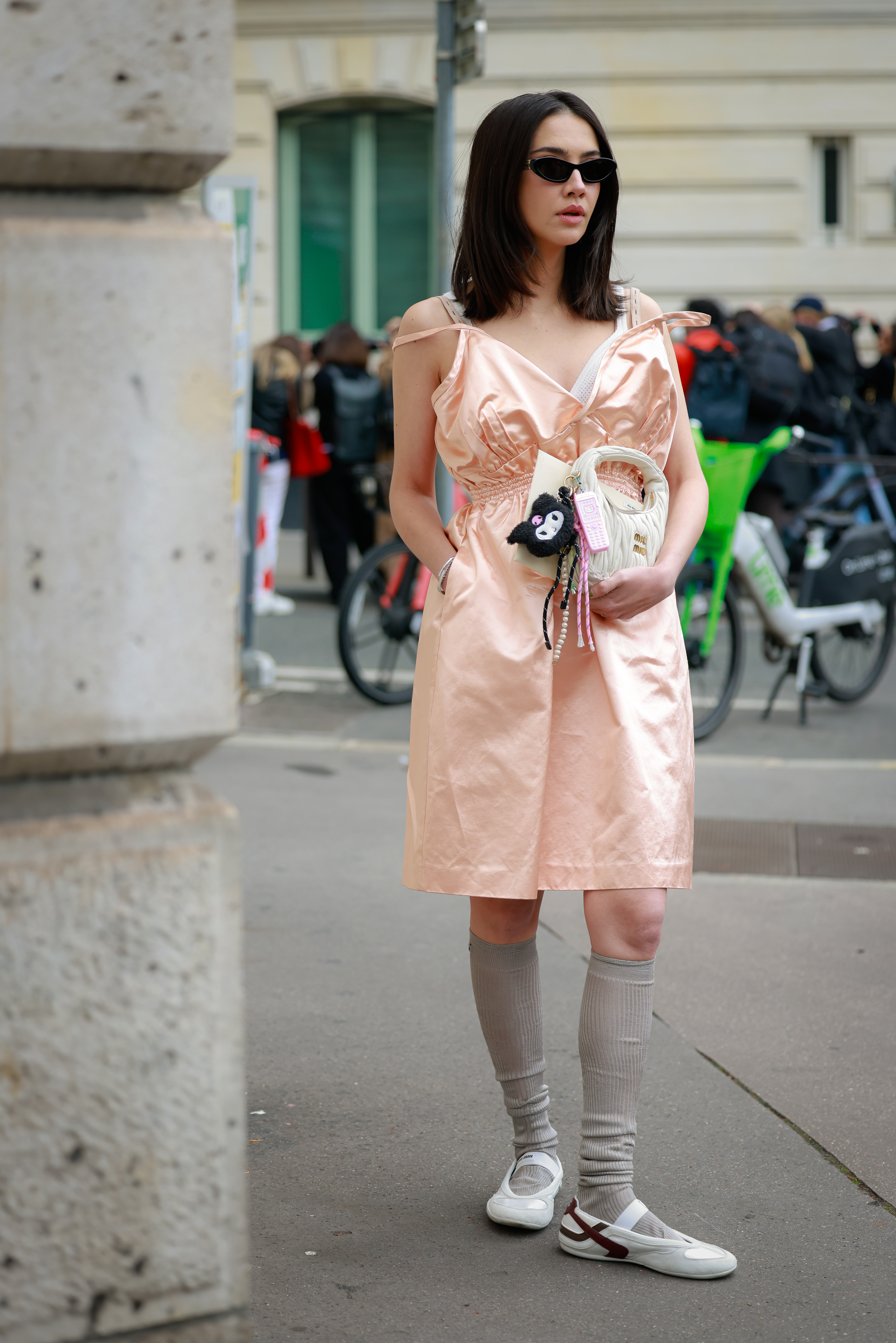 PARIS, FRANCE - OCTOBER 06: A guest is seen wearing black sunglasses, apricot-pink silky midi dress, white Miu Miu bag, grey socks and white sneakers outside Miu Miu during the Womenswear Spring Summer 2026 as part of Paris Fashion Week on October 06, 2025 in Paris, France. (Photo by Hanna Lassen/Getty Images)