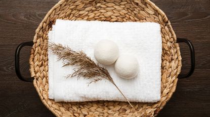 Two wool dryer balls on a white towel beside a piece of wheat, on a rattan table mat