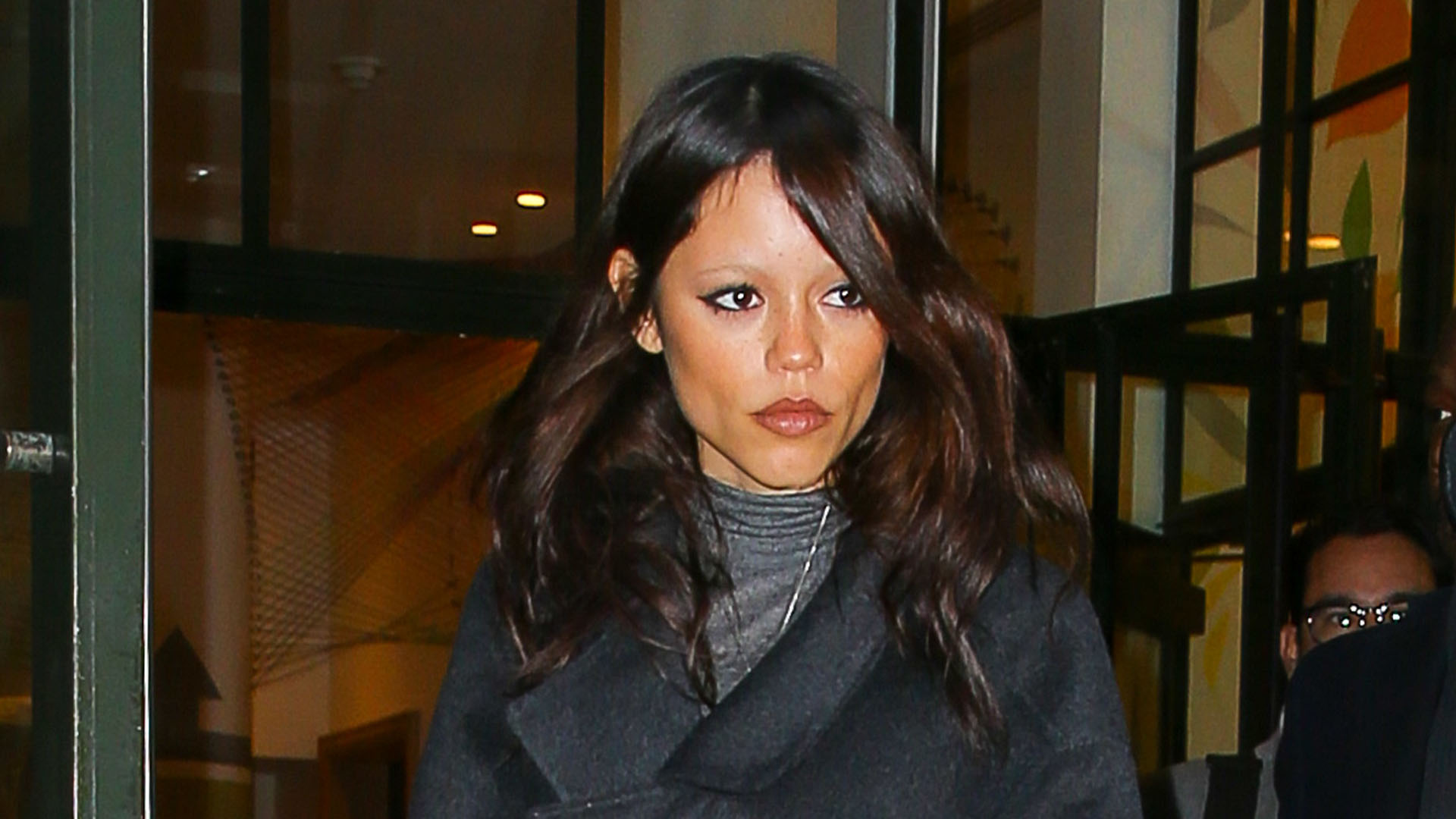 Jenna Ortega wearing a black coat and jeans