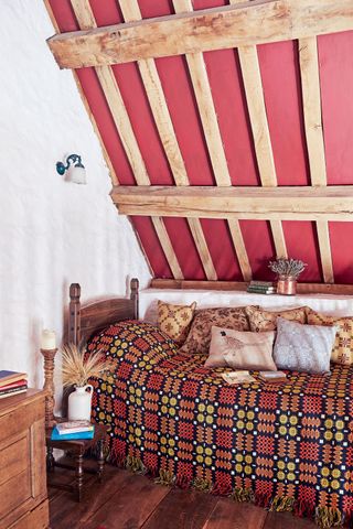 bedroom with red welsh blanket under eaves in farmhouse mezzanine with beams and limewashed walls