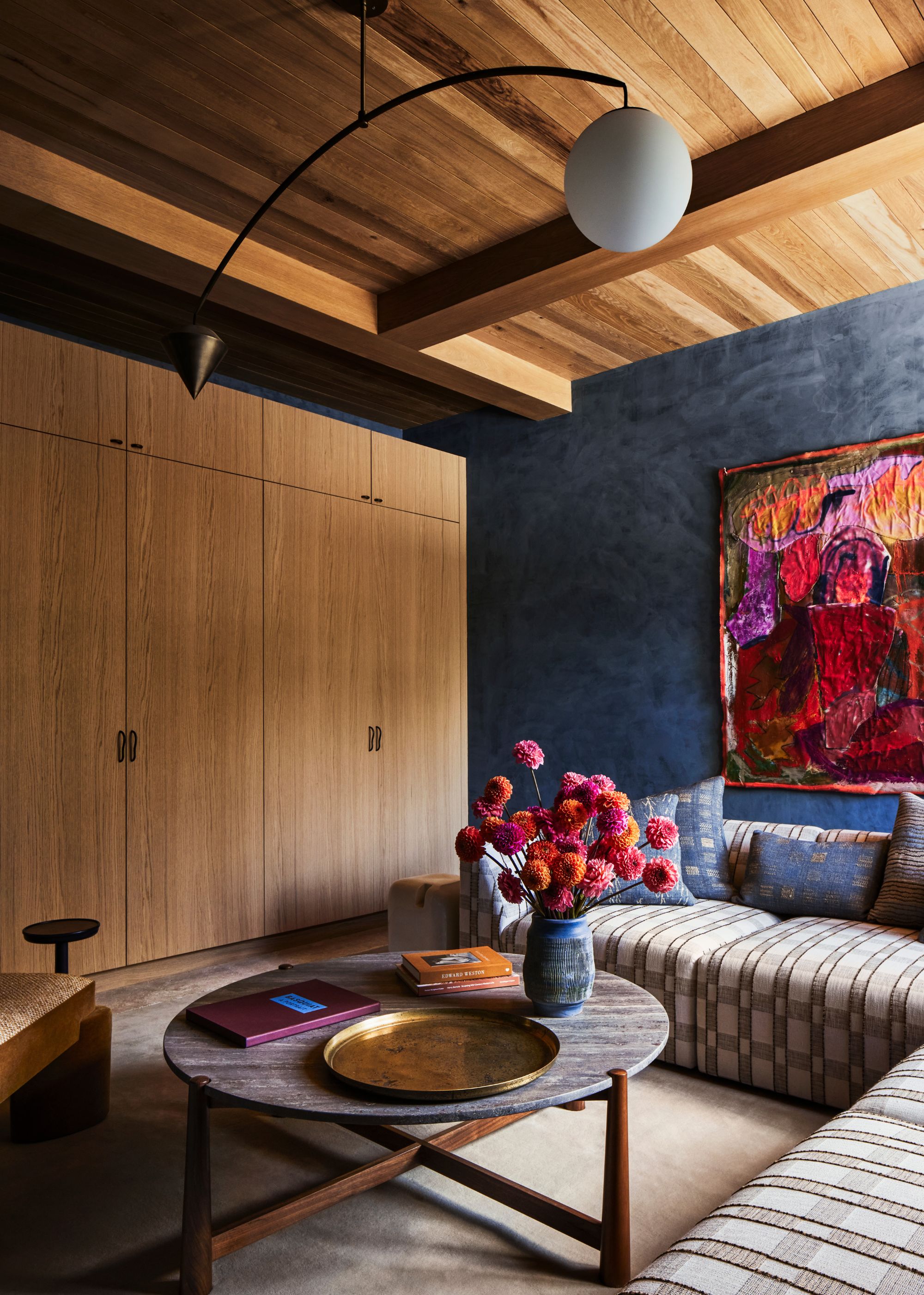 Living room with wood-clad walls in a golden honey tone, a corer sofa and blue wall.