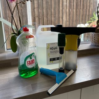 Bottles of washing up liquid and white vinegar sitting on kitchen worktops next to a Dishmatic, Karcher window vac and a blue squeegee