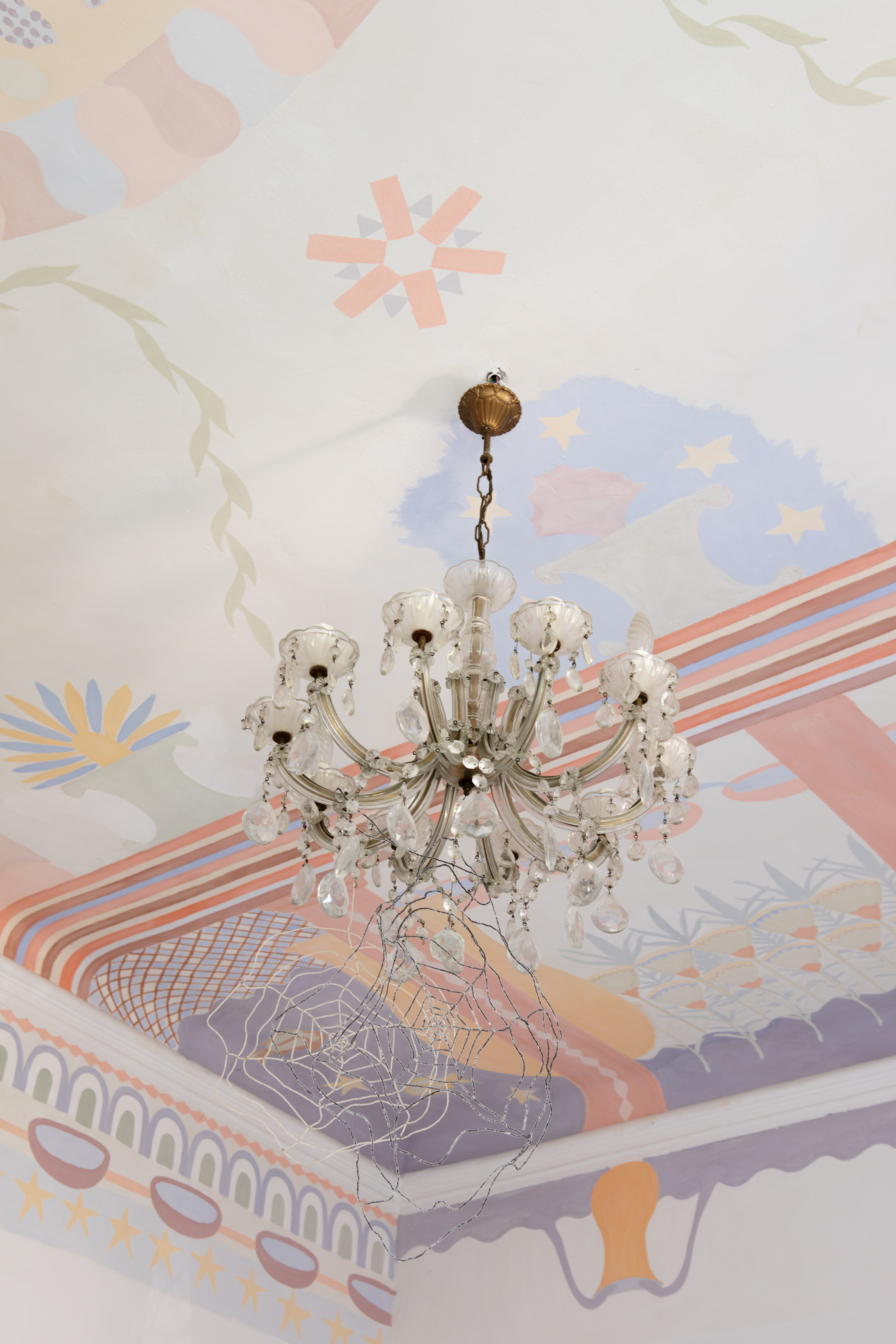 A beautifully renovated, palatial building with frescoed ceilings and walls houses an array of gothic-inspired furniture that simultaneously nod to contemporary and classical design, including tapestries, chandeliers, and velvety seats, and wooden decor.
