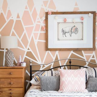 bedroom with pink geometric wall and wooden chest of drawers