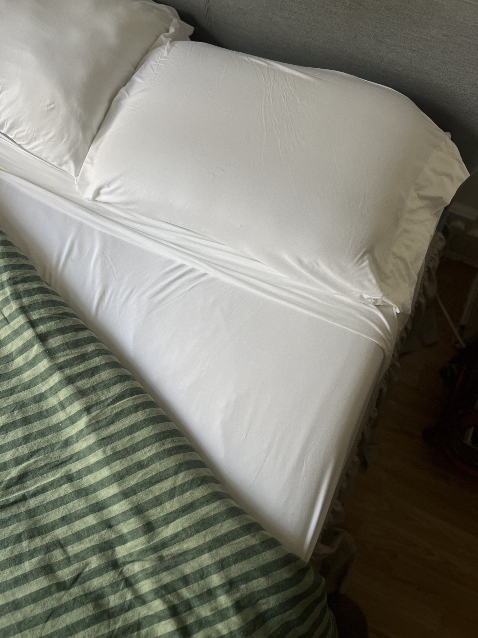Image of a bed with a green striped turned down to show white sheets.